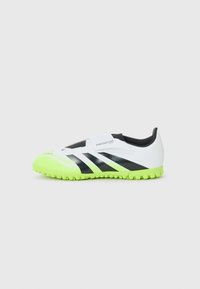 Botas de fútbol blancas y negras con una suela de goma verde. Presentan un diseño elegante, parte superior texturizada y una correa ajustable para el ajuste.