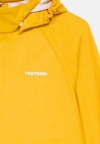 Jacket amarela à prova d'água com um colarinho alto, capuz ajustável e logo branco "TRETORN". Textura lisa e um design moderno e elegante.