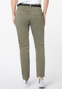 Olijfgroene tapered broek met een gladde textuur, elastische tailleband en twee achterzakken. Gecombineerd met witte sneakers met gekleurde accenten.