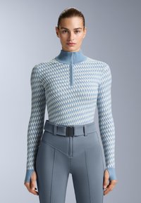 Ljusblå zip-uptröja med ett strukturerat geometriskt mönster, i kombination med högmidjade figurnära byxor och ett brett bälte.