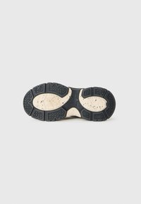 Suela de una bota de trabajo con patrones de tracción negros sobre una base beige, con un agarre texturizado y una forma de estrella en el centro.