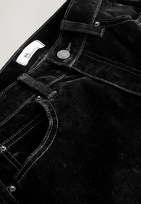 Zwarte corduroy broek met rechte snit, voorzien van een metalen knop, label en contrasterende witte stiksels. Zacht, textuurachtig stof.