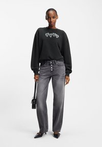 Juodas megztinis su „HUGO“ logotipu širdelių formos. Pilkos džinsės su penkių mygtukų priekyje, tiesaus kirpimo ir subtilaus išblukimo. Juoda rankinė ir batai.