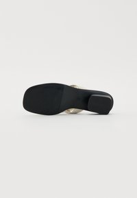 Semelle en caoutchouc noir avec texture antidérapante, sangles supérieures beiges et talon carré. Design minimaliste avec une finition lisse et des bords arrondis.