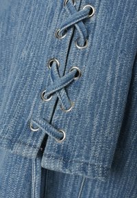 Denim tkanina u svijetloplavoj boji s suptilnim okomitim prugama. Sadrži srebrne rupice i detalj križnog vezivanja za učvršćivanje.