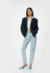 Marinblå överdimensionerad kavaj, vit kort topp, slitna ljusblå jeans och ljusblå stilettklackar. Synliga detaljer med knappar och krage.