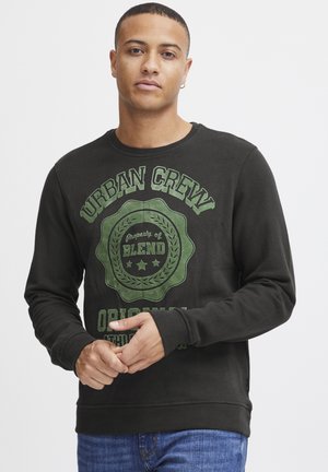 Black crewneck sweatshirt with green graphic text and emblem, long sleeves, textured fabric. Worn with blue denim jeans.