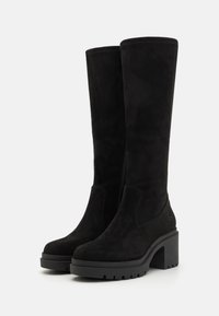 Bottes noires en daim hautes aux genoux avec un talon plateforme épais, fermeture éclair sur le côté et un logo subtil. Texture lisse et silhouette ajustée.