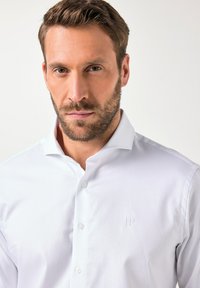 Camicia bianca con bottoni in tessuto testurizzato, dotata di colletto classico, bottoni a vista e logo ricamato sul petto.