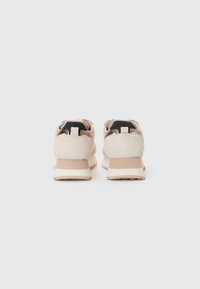Beige sportieve schoenen met een gestructureerde suède bovenkant, een zwarte hiel lus en een chunky witte zool met lichtbruine accenten.