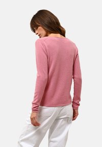 Maglione rosa chiaro a maniche lunghe realizzato in materiale morbido, con scollatura rotonda e maniche aderenti, indossato con pantaloni bianchi.