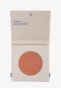 Kompaktfodral med en rund panna av matt terrakotta-blush, märkt "INFUSERAD MED Pionblomsextrakt, naturligt ursprung estrar."