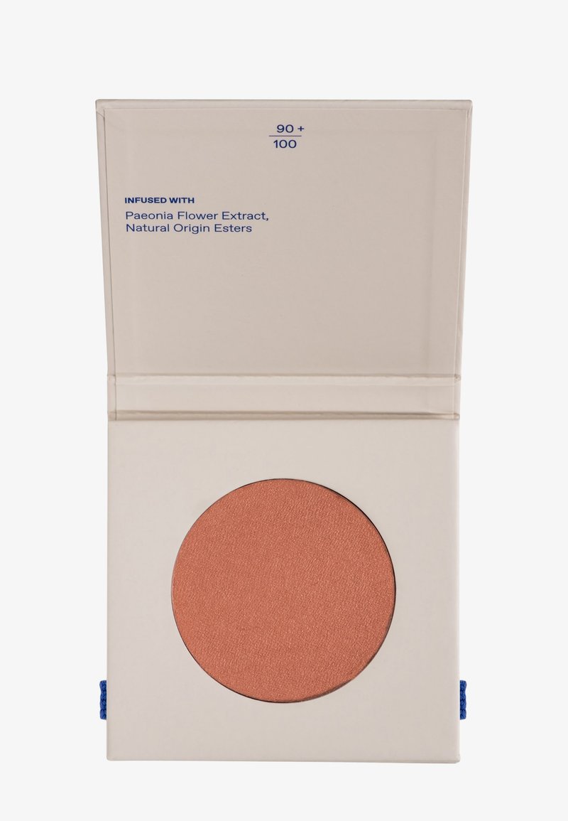 Kompaktfodral med en rund panna av matt terrakotta-blush, märkt "INFUSERAD MED Pionblomsextrakt, naturligt ursprung estrar."