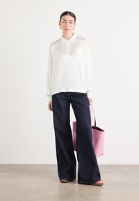 Chemise blanche à manches longues avec des boutons, jeans larges noirs, et un sac fourre-tout rose. Tissu lisse et design décontracté avec des accents minimaux.