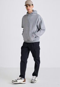 Grå hettegenser med løs passform, sammen med mørke cargo-bukser og hvite sneakers med brune detaljer. Caps i lys beige.