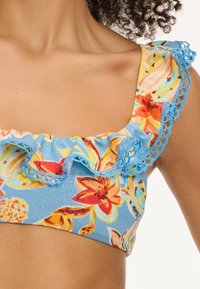 Modra cvetlična bikini vrhnja z nabranimi robovi. Ima živahne oranžne, rumene in zelene cvetove, okrašene z modrimi čipkastimi detajli.