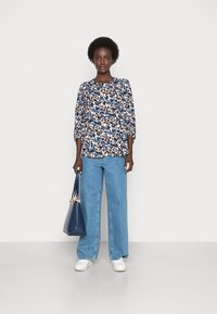 Blusa com padrão floral em azuis, rosas e creme; jeans de perna larga em denim; bolsa azul-marinho; ténis brancos; tecido leve e suave; corte relaxado.