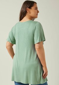 Grön, kortärmad, crew-neck tröja med avslappnad passform; slät, lättviktig tygkvalitet; har en längre bakdel och subtil textur.