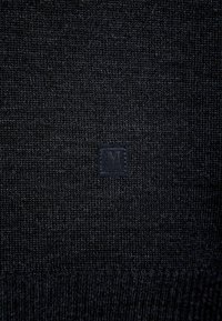 Dunkel gestrickter Pullover mit einer subtilen Textur und einem kleinen, quadratischen schwarzen Logopatch auf der Vorderseite, der ein sauberes Design betont.