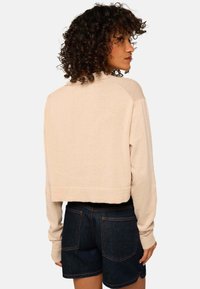 Pull en beige à col ras du cou, ajusté et à manches longues. Texture douce. Associé à un short en denim foncé avec poches arrière et coutures visibles.