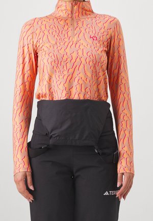 Langærmet t-shirt med fersken- og pink abstrakt mønster med en kvart lynlås, kombineret med sorte højtaljede bukser med frontklap og sidelommer.