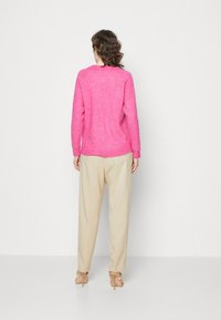 Rosa stickad tröja med rund halsringning, långa ärmar och avslappnad passform, matchad med krämfärgade lösa byxor och nakna klackar.