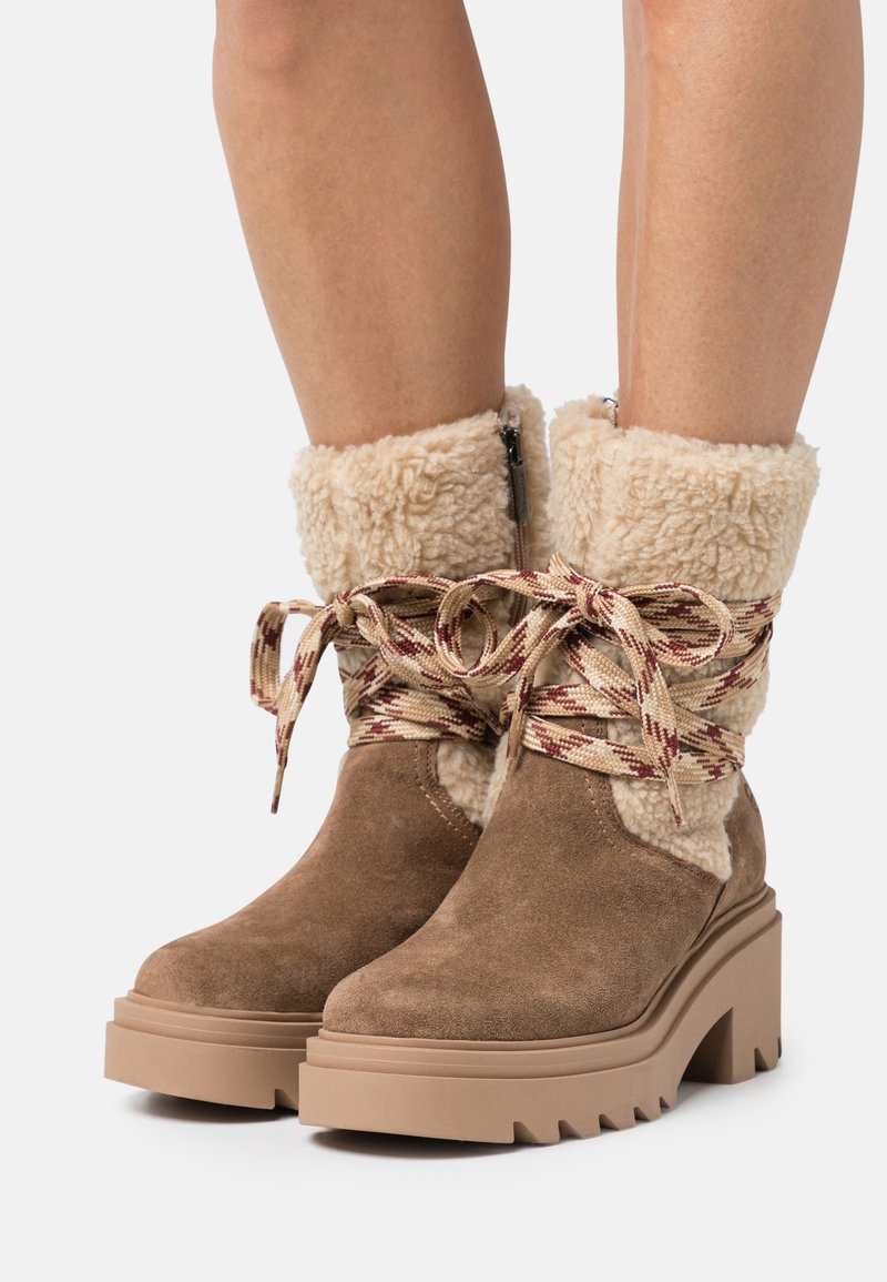 Brązowe zamszowe botki za kostkę z sztucznym futerkiem, grubą platformą i zygzakowatą podeszwą; posiadają wzorzysty sznurowanie i zamek błyskawiczny z boku.