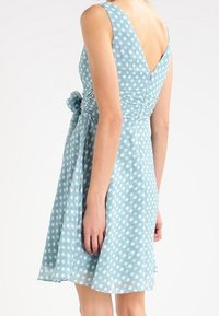 Helles blaues Kleid mit Polka-Dots, V-Ausschnitt, figurbetontem Oberteil und A-Linie-Rock, mit einer Rückenkrawatte und weichem, strukturiertem Stoff.