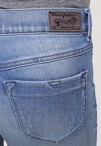 Ljusblå denimjeans med en läderetikett på midjebandet, en bakficka med en triangulär sömdetalj och en sliten textur.