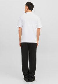 White short-sleeve t-shirt with a crew neckline, paired with black loose-fitting trousers and black footwear, viewed from the back.