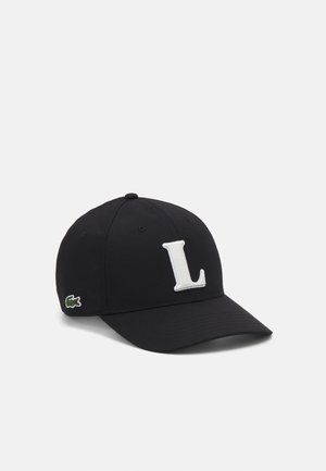 Juoda kepurė su lenktu kraštu, ant kurios priekyje yra didelė balta siuvinėta "L" raidė ir žalia Lacoste logotipas šone.