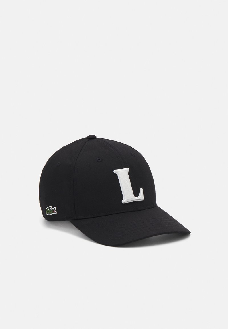 Casquette noire avec un visière courbé, arborant un grand "L" blanc brodé à l'avant et un logo Lacoste vert sur le côté.