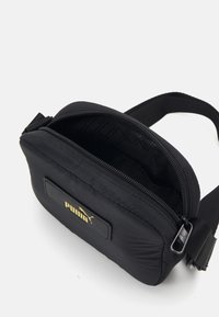 Czarna nylonowa torba na ramię z złotą naszywką z logo, zamknięciem na zamek, pikowaną teksturą oraz regulowanym paskiem; wnętrze posiada wzorzystą podszewkę.