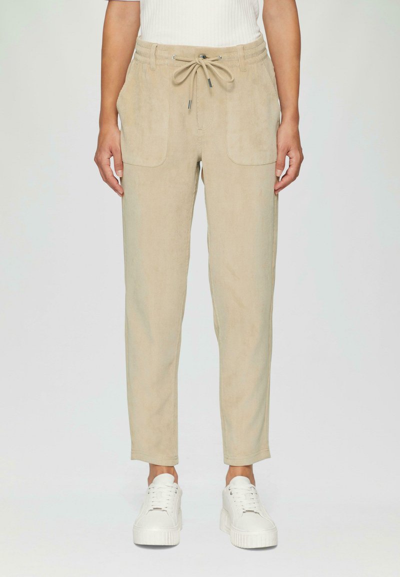 Beige corduroy broek met een trekkoord in de taille, twee voorzakken en een tapered pasvorm. G gedragen met witte sneakers.