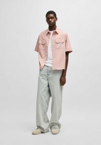Korte mouwen roze shirt met twee voorzakken, gecombineerd met lichtgekleurde wijde jeans en beige sneakers. Minimalistisch ontwerp en losse pasvorm.