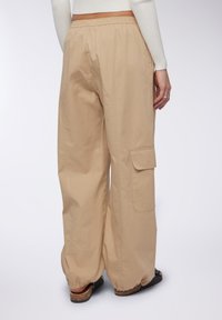 Pantaloni cargo beige realizzati in tessuto leggero, con vita regolabile mediante coulisse, tasche laterali e polsini elasticizzati.