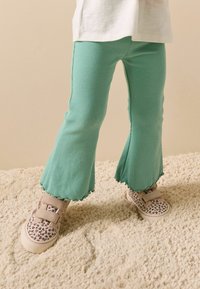 Világos türkiz színű bordázott, bővülő szabású nadrág fodros szegéllyel; bézs színű, leopárdmintás és dupla tépőzáras sportcipővel párosítva.