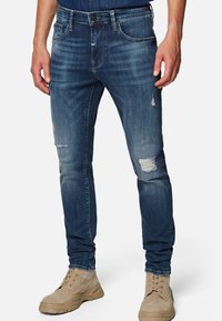 Fitted dark blue jeans with a distressed texture, featuring frayed rips at the knees and classic five-pocket design.