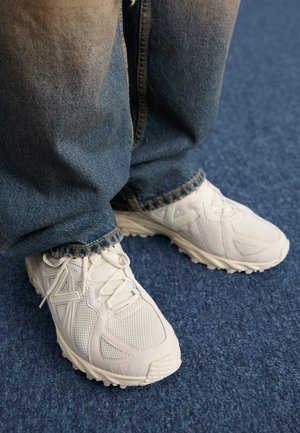 Hvide atletiske sneakers med tekstureret mesh-overdel, gummisåler og minimale brandingdetaljer. Sammen med løse denimjeans.