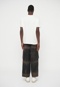 Λευκό κοντομάνικο μπλουζάκι σε συνδυασμό με χαλαρές, μαύρες cargo παντελόνες με καφέ λεπτομέρειες και πλαϊνές τσέπες, συνδυασμένο με λευκά αθλητικά παπούτσια.