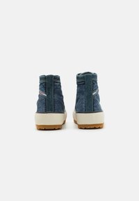 Botas de tornozelo em denim azul com um tecido texturizado, sola de borracha castanha em contraste e um colarinho acolchoado. Apresenta um detalhe de costura vertical e logotipo.