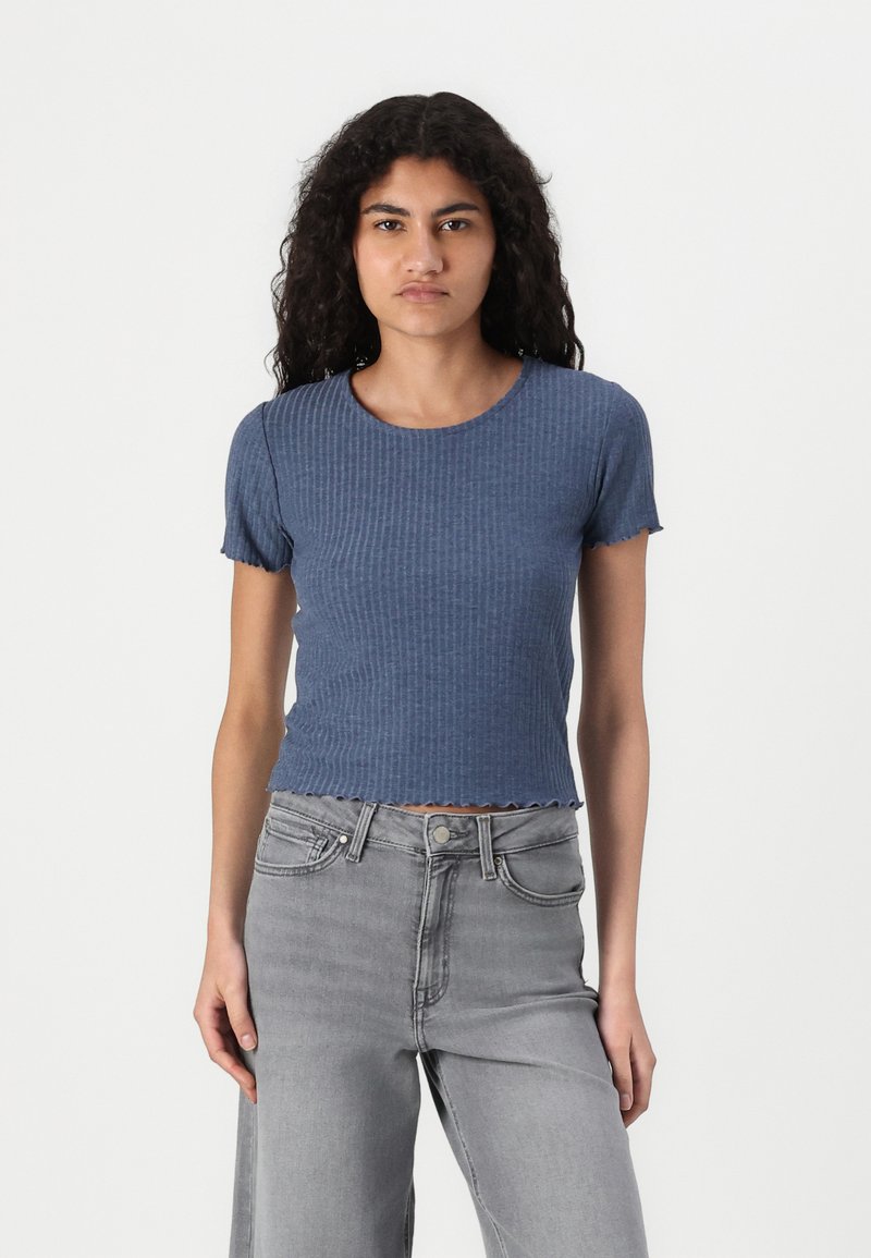 Blå randig kortärmad topp med rund halsringning och vågig nederkant, i kombination med ljusgrå jeans. Tyget verkar mjukt och texturerat.