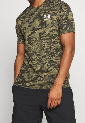 Mann trägt ein olivgrünes digitales Tarn-Unter-Armour-T-Shirt und schwarze Shorts, steht mit einer Hand in der Tasche und der anderen entspannt.