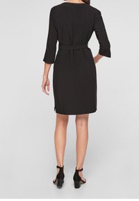 Robe noire à manches trois-quarts, taille ceinturée et longueur au genou. Tissu lisse avec un design simple et épuré.