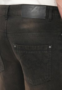 Μαύρο τζιν από denim με ετικέτα ζώνης από δέρμα με υφή, διακριτική ραφή στην πίσω τσέπη και ελαφρώς φθαρμένη εμφάνιση.