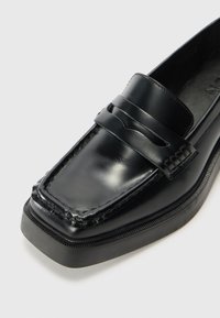 Sorte skinnloafers med avrundet tå, med et dekorativt bånd over foran, teksturert søm og gummisåle.