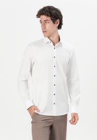 White long-sleeve shirt made of smooth fabric; features a classic collar and black buttons down the front; fitted design.