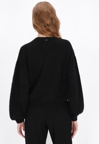 Sort, oversized striktrøje med en tekstureret finish, brede ballonærmer og ribbede kanter, med en diskret bagetikette.