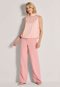 Blouse met verticaal lichtroze en witte strepen, geplooide halslijn; gecombineerd met lichtroze wijde broek. Beige puntige schoenen.