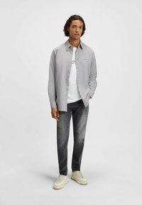 Grau kariertes Hemd mit weitem Kragen, kombiniert mit einem weißen Grafik-T-Shirt, grauen Jeans und hellen Sneakers.